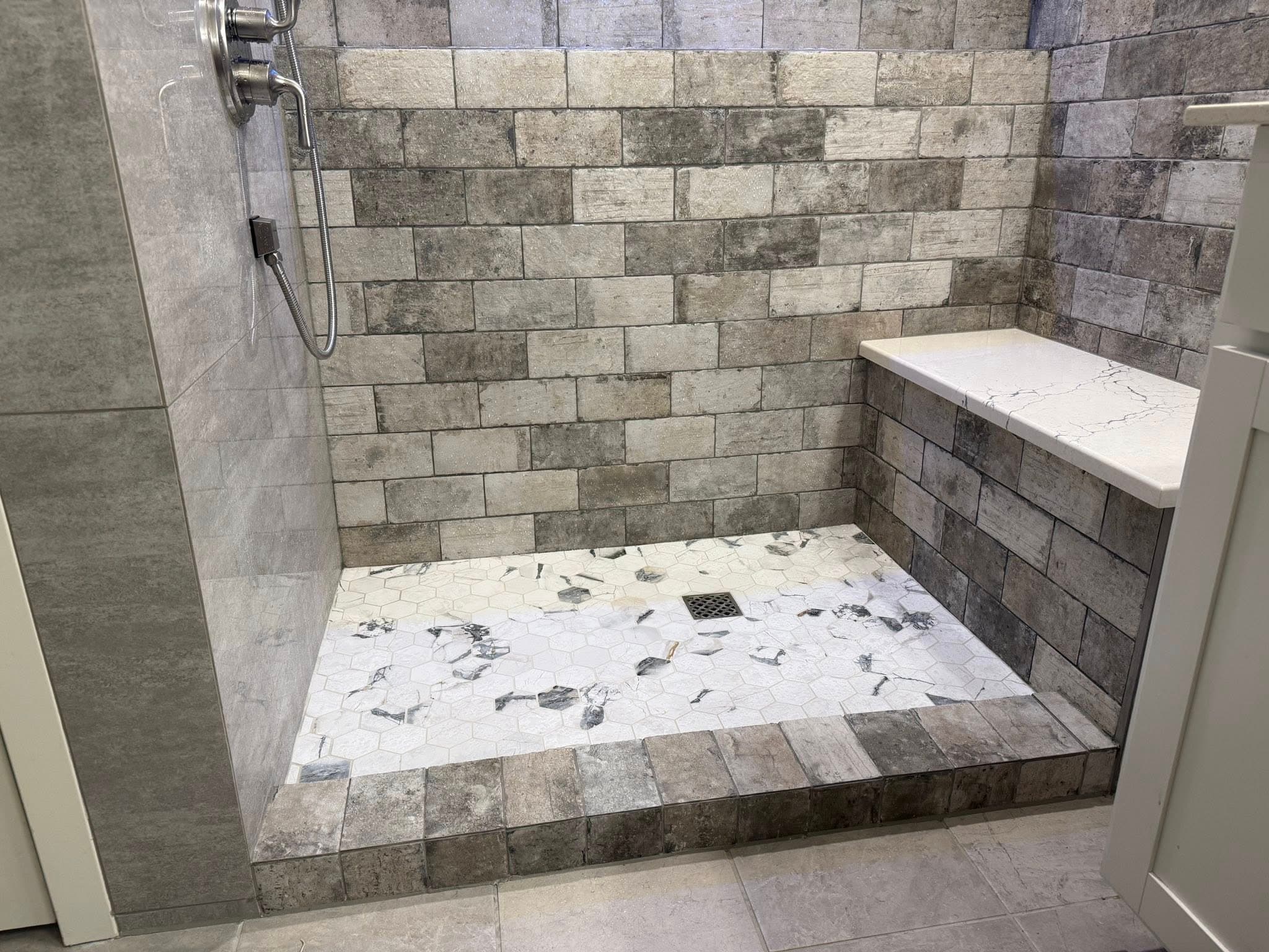Wide gray brick shower with marble pebble floor by NOCO Tile